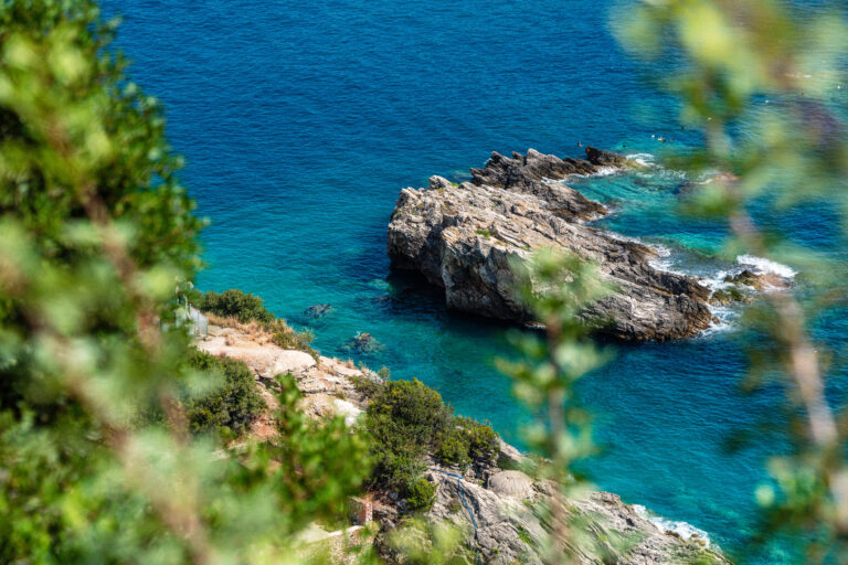 blue waters with large rock framed by green tree branches