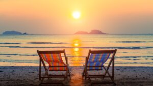 beach chairs facing sea with sun setting in background